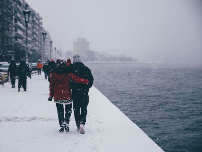 People walking on snow covered pier by sea against sky