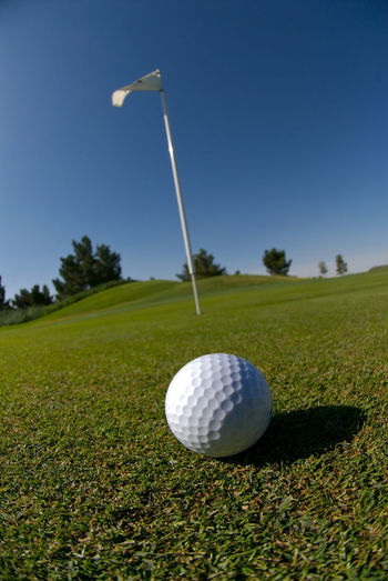 Close-up of ball on golf course against clear blue sky