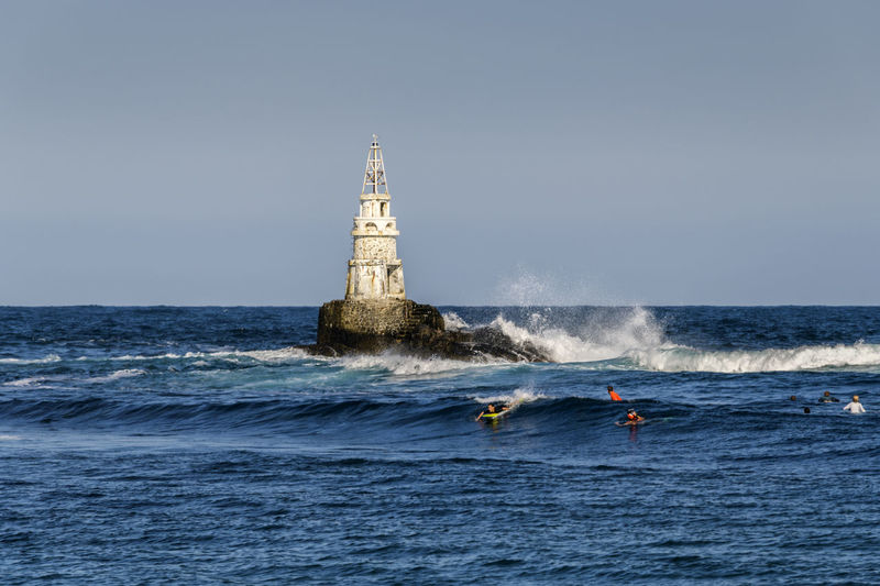 Lighthouse on sea by building against clear sky
