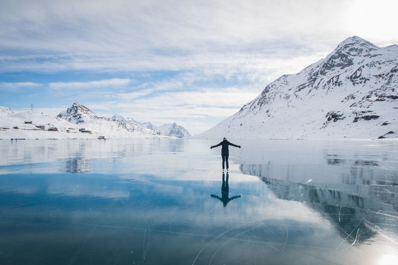 Woman standing on frozen lake by snowcapped mountain against cloudy sky