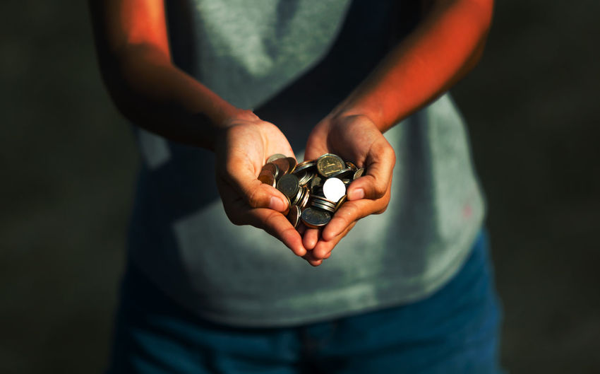 Midsection of person holding coins in cupped hands