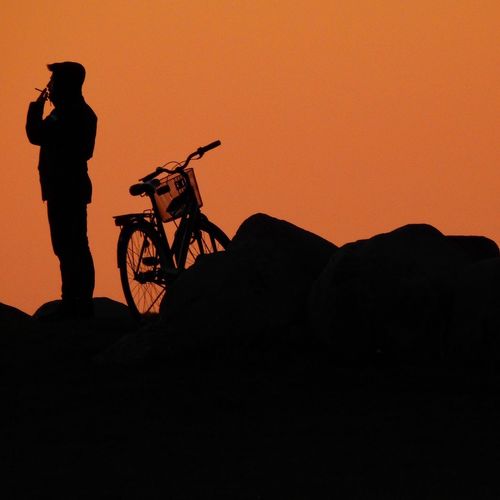 Silhouette man riding bicycle on cliff during sunset