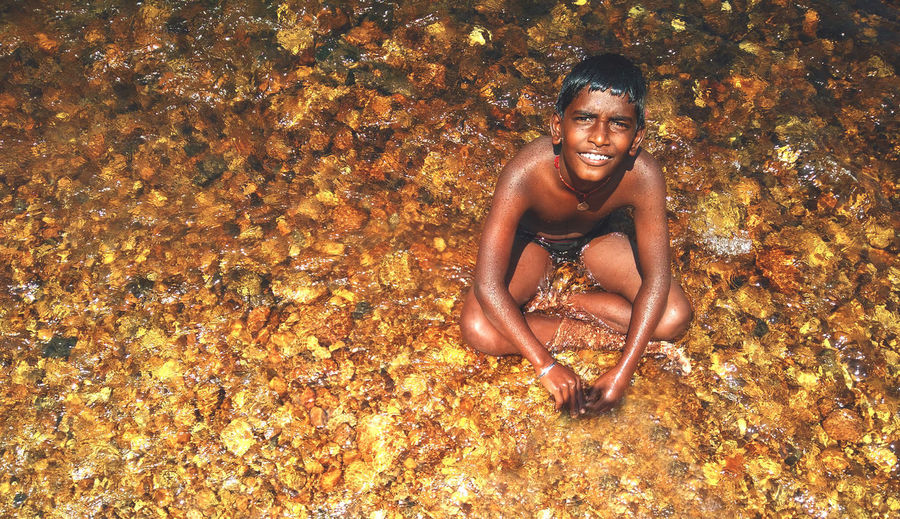 High angle portrait of happy shirtless boy sitting in stream