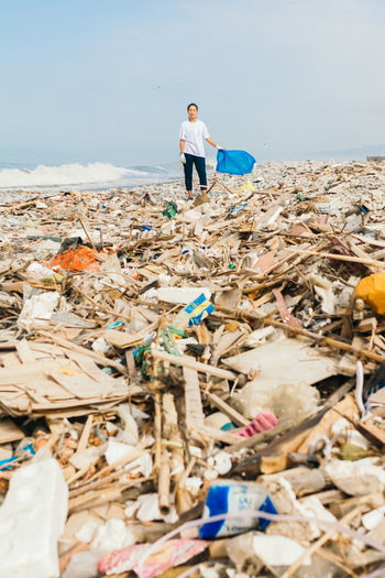  latin woman holding a blue bag over a pile of garbage and trash on a polluted beach. 