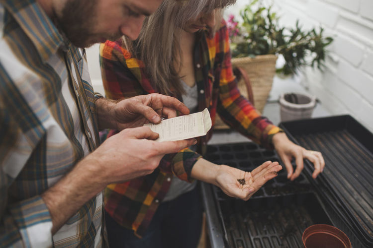 Man reading instruction while woman sprinkling seed on seedling tray