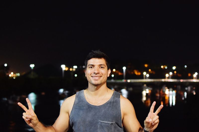 Portrait of man smiling while gesturing peace sign in city at night