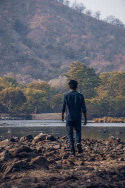 Rear view of man walking at riverbank against mountain