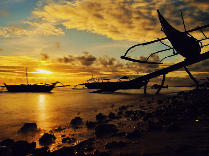 Silhouette boats moored on beach against sky during sunset