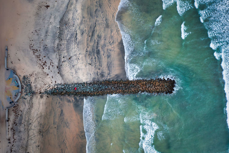 Overhead top-down dramatic drone view of jetty with waves breaking.