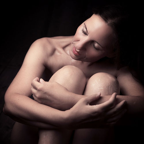 Portrait of shirtless young woman sitting against black background