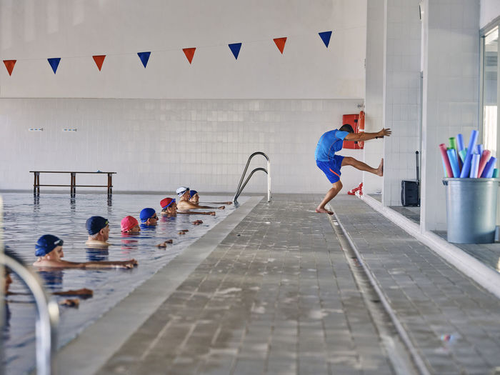 Side view of company of people in swimwear doing exercises with trainer during water aerobics in swimming pool