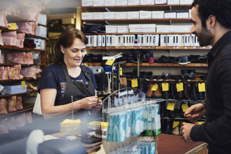 Smiling customer looking at shoemaker reading name tag in shop