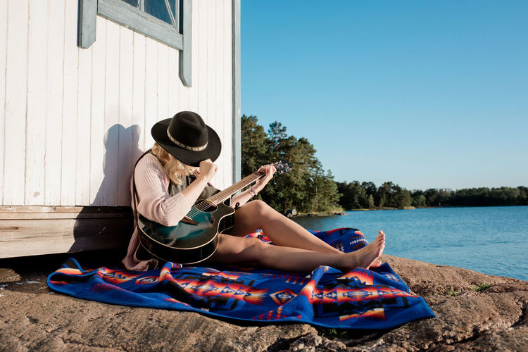 Woman sat with a hat on sunbathing in the sun playing the guitar