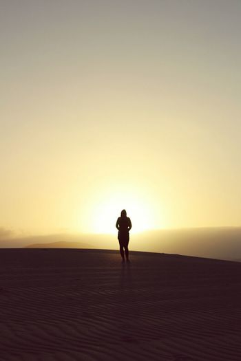 Silhouette woman standing on desert against sky during sunset