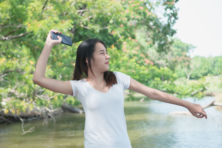 Full length of young woman standing against trees
