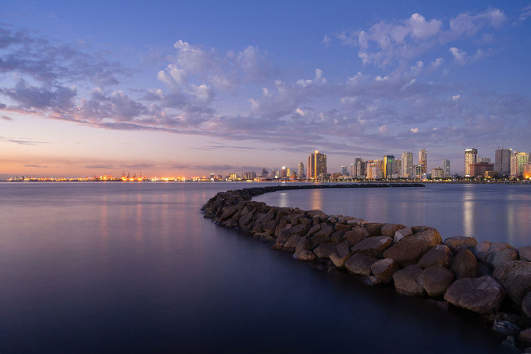 Illuminated city at waterfront against sky