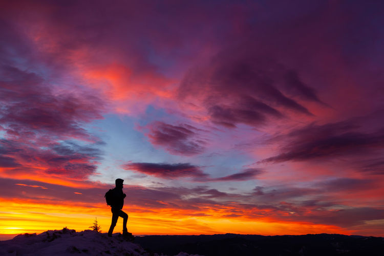 Silhouette of a man on mountain with a colorful sunset sky above.