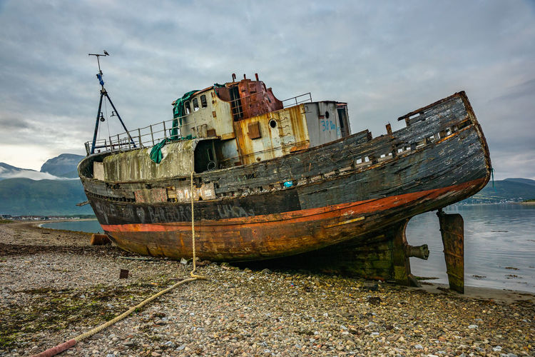 Abandoned boat moored at shore against sky