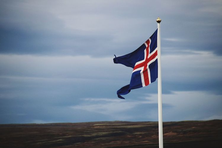 Low angle view of icelandic flag on pole against sky
