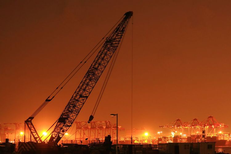 Cranes at commercial dock against sky during sunset