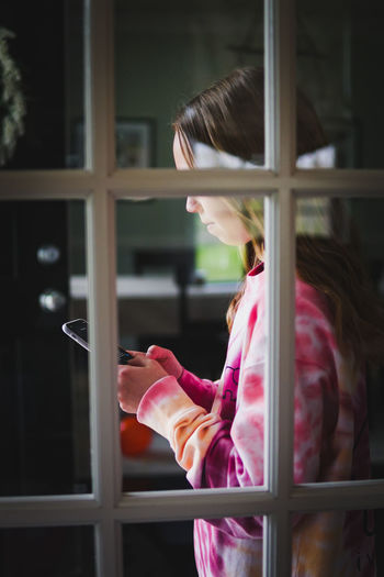 Side view of girl using smart phone seen through window