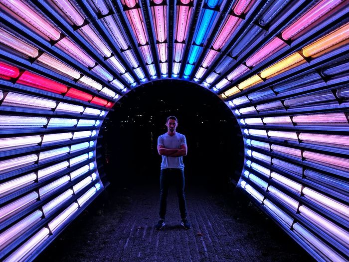 Man standing in colorful illuminated tunnel at night