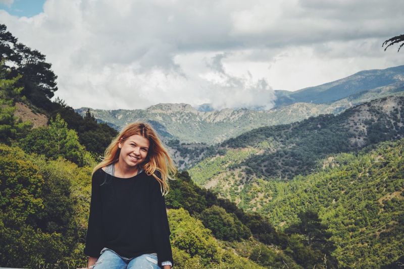 Portrait of smiling young woman sitting against mountain ranges