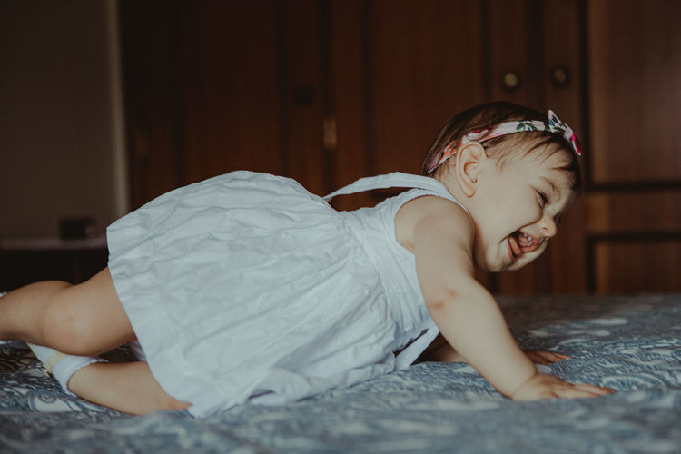 Side view of cute baby girl lying on bed at home