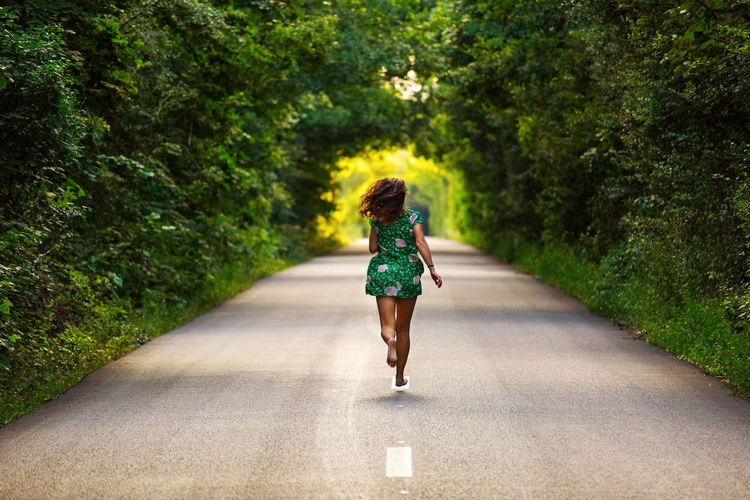 Rear view of woman running on road amidst trees