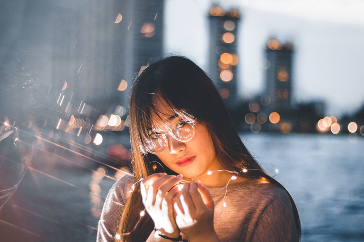 Portrait of woman holding illuminated string lights in city