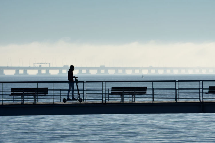 Silhouette man standing by railing against sea
