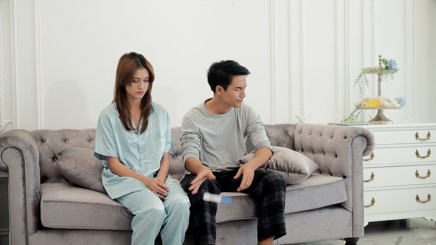 Sad couple throwing pregnancy test while sitting on sofa