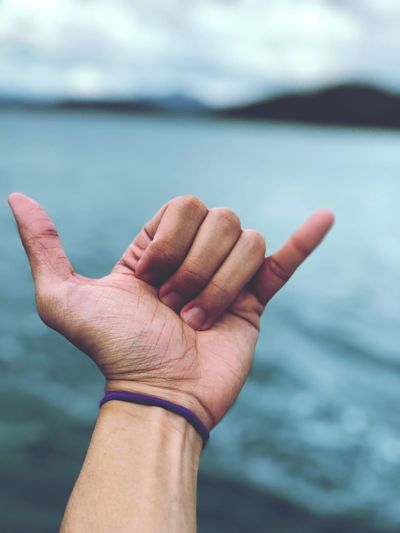 Cropped hand gesturing shaka sign against sea