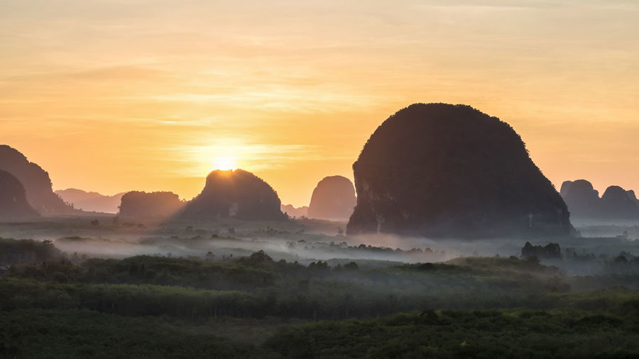 Panorama sunrise beam rays through silhouette limestone mountains and mist in krabi
