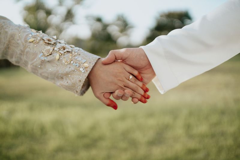 Cropped image of bride and bridegroom holding hands on field