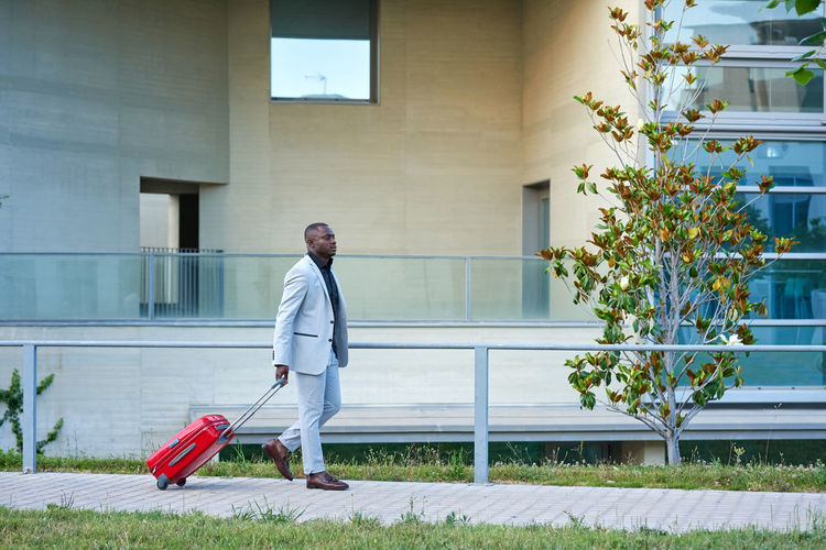 African-american in a white suit and a red suitcase.