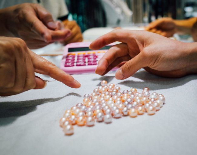 Cropped hands of people counting pearls on desk