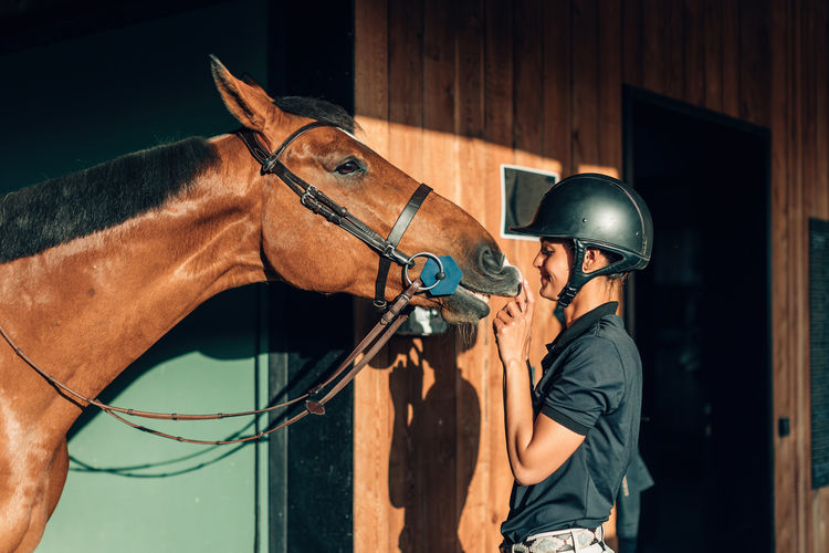 Female professional rider bonding with her horse - thoroughbred connecting and smiling to her human