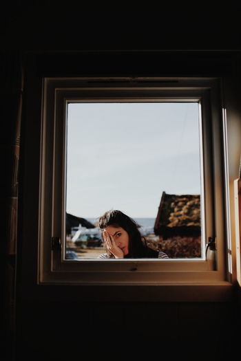 Portrait of woman looking through window at home