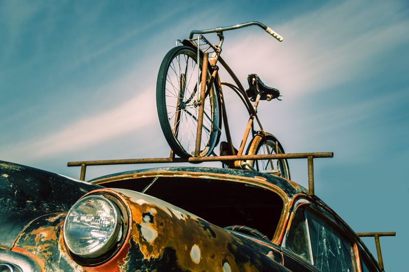 Bicycle on abandoned car against sky