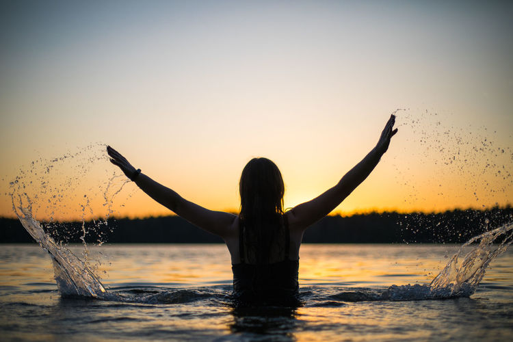 Silhouette man with arms outstretched standing in sea against sky during sunset
