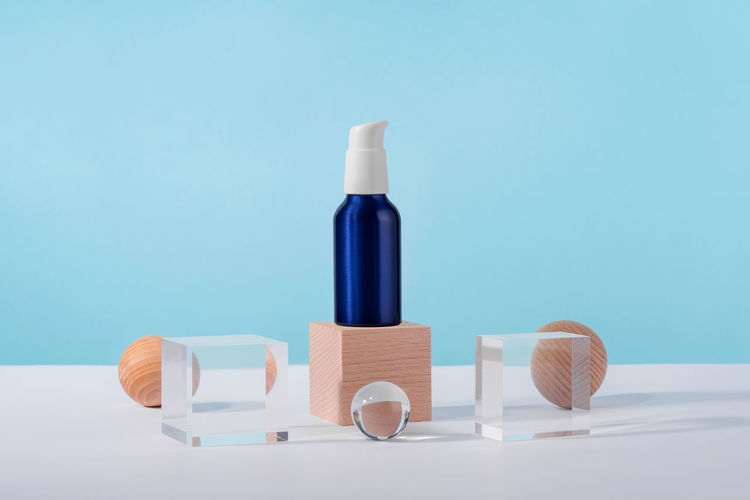 Cosmetic cream metallic pump bottle mockup on blue background with stylish props on acrylic pedestal
