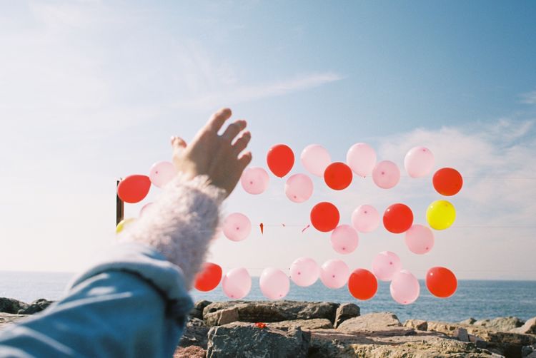 Cropped hand of woman gesturing against helium balloons on rocky shore