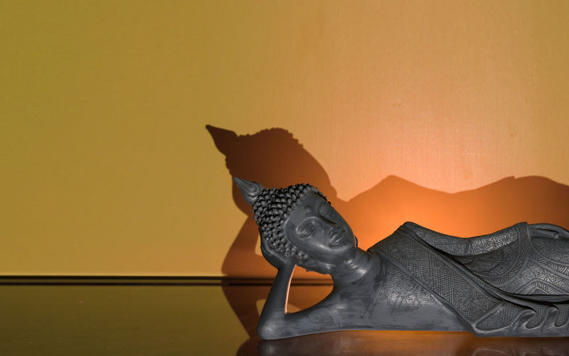 Low section of cat by statue against orange wall