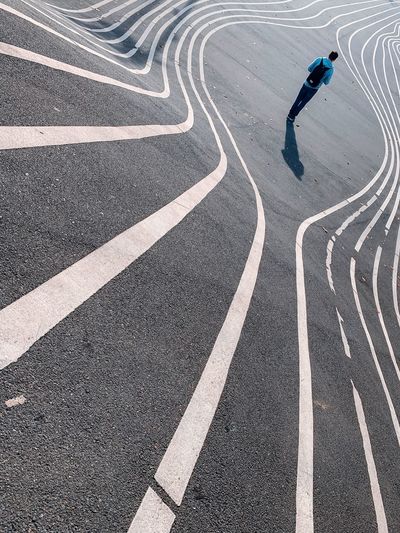 Rear view of man walking on road with markings