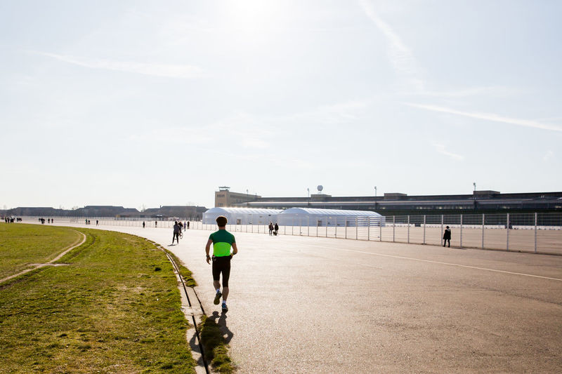 Rear view of man jogging on road against sky at tempelhofer feld during sunny day