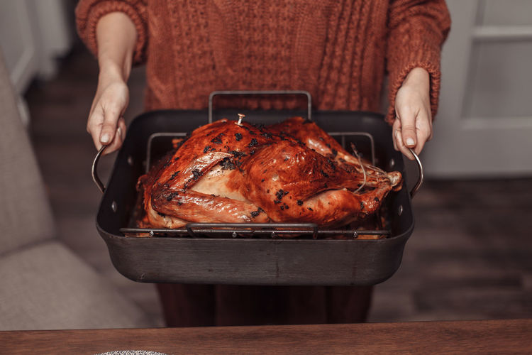 Woman holding metal tray with roasted turkey
