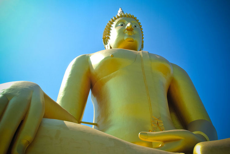 Low angle view of buddha statue against blue sky
