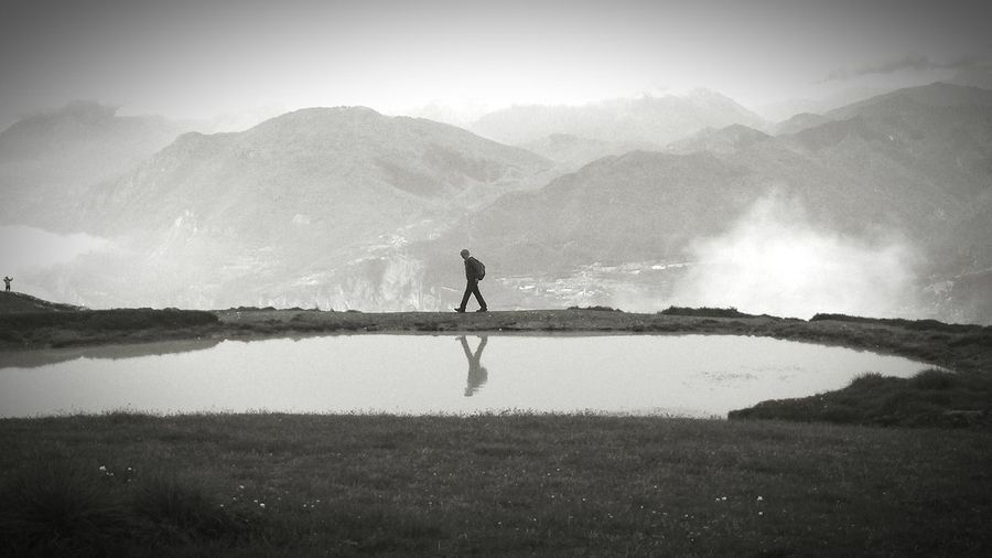 Side view of man walking by pond against monte baldo