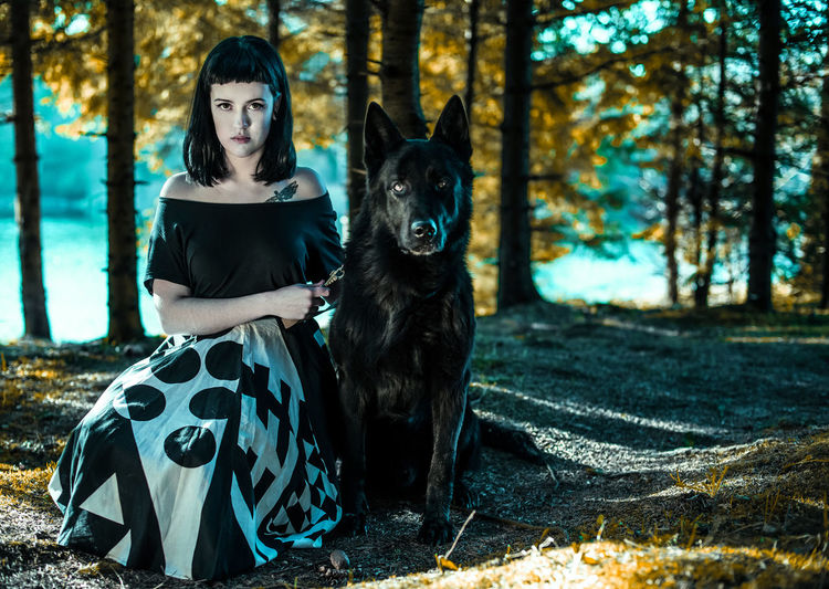 Portrait of young woman crouching by black shepherd in forest